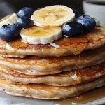 A stack of Kodiak Cakes pancakes with blueberries, bananas, and syrup.